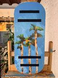 Tabla de equilibrio Balance Surfers de madera hecha a mano en taller de Barcelona. Palmeras pintadas sobre madera natural mientras la artista hacía equilibrio sobre otra balance board. 