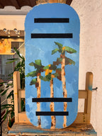 Tabla de equilibrio Balance Surfers de madera hecha a mano en taller de Barcelona. Palmeras pintadas sobre madera natural mientras la artista hacía equilibrio sobre otra balance board. 