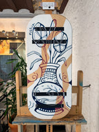 Tabla de equilibrio Balance Surfers pintada a mano por la artista Nahia, con una ilustración de un jarrón ornamental y flores en trazo azul sobre un fondo geométrico de tonos crema, blanco y granate en madera de abedul. 