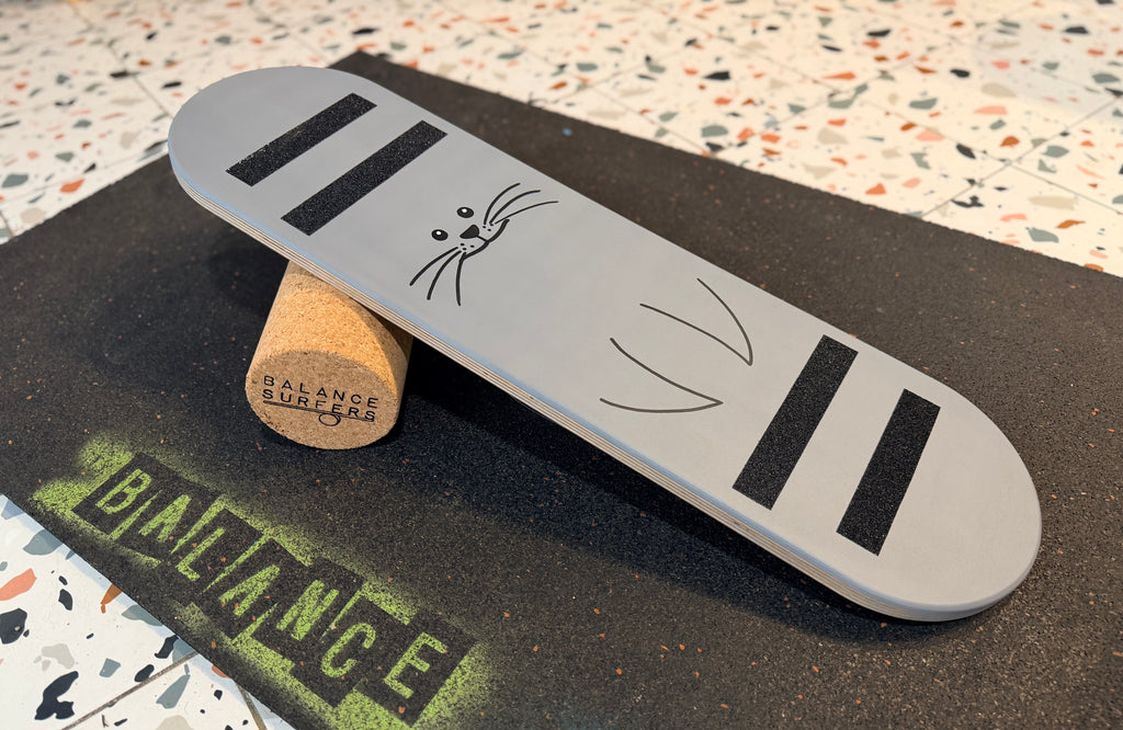 Tabla de equilibrio infantil Balance SurfKids pintada a mano en color gris claro con la ilustración de una foca y cuatro bandas antideslizantes negras sobre madera de abedul natural
