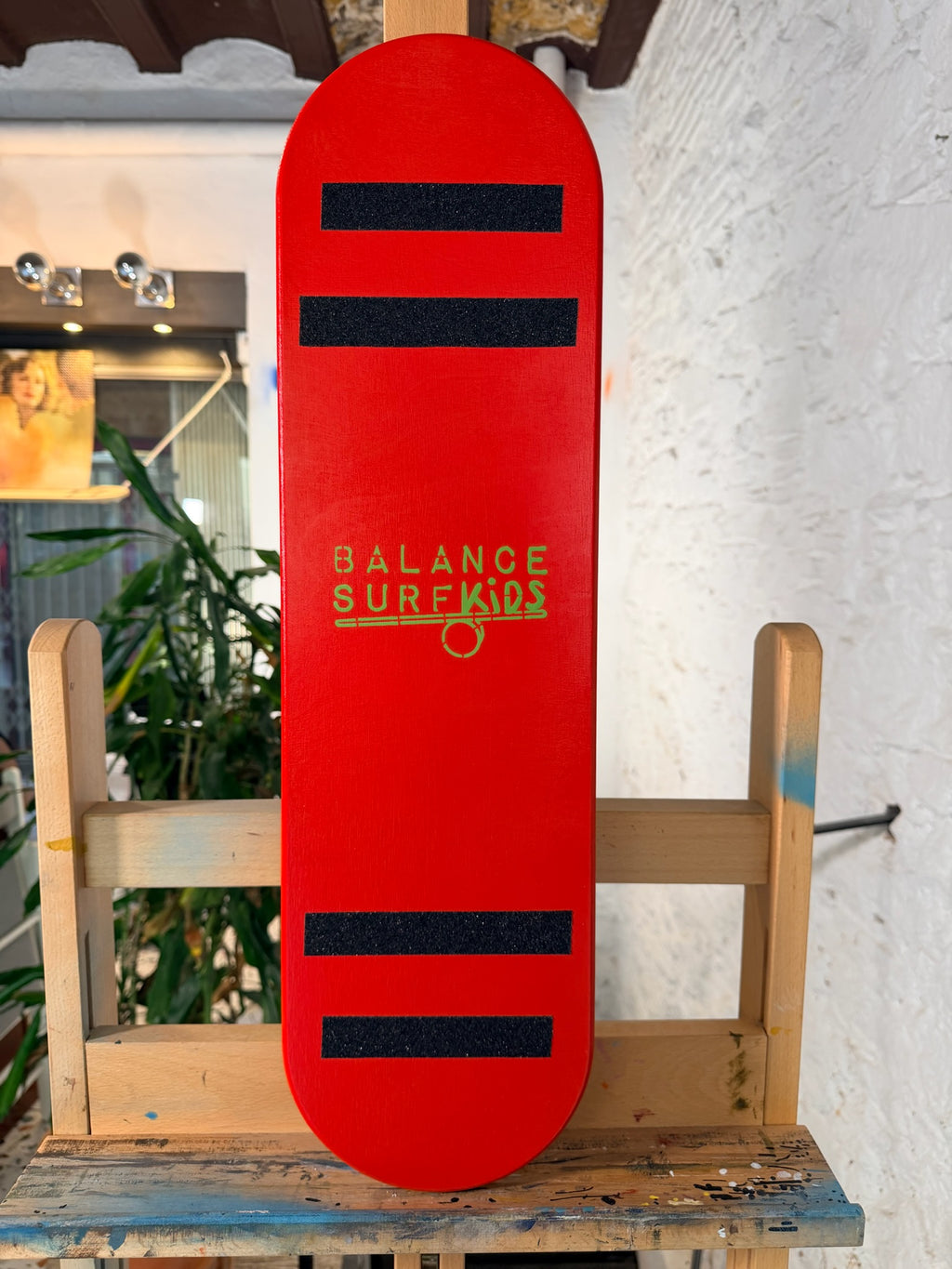 Tabla de equilibrio para niños roja con logo en verde sobre caballete. Handmade Balance board 