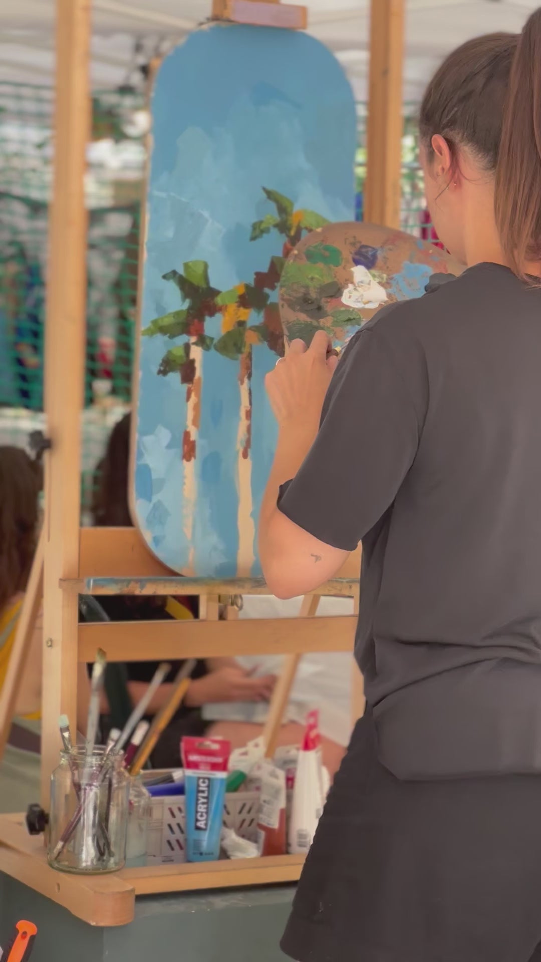 Artista pintando con acrílico una tabla de equilibrio o balance board de madera ecológica natural mientras hace equilibrio sobre otra tabla. 